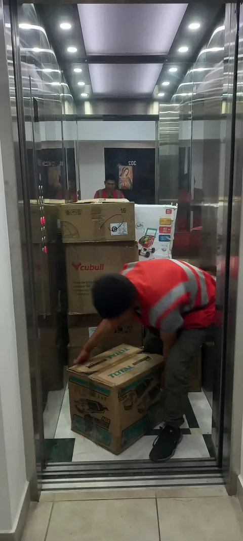 Cargador con chaleco subiendo cajas en el ascensor de un edificio