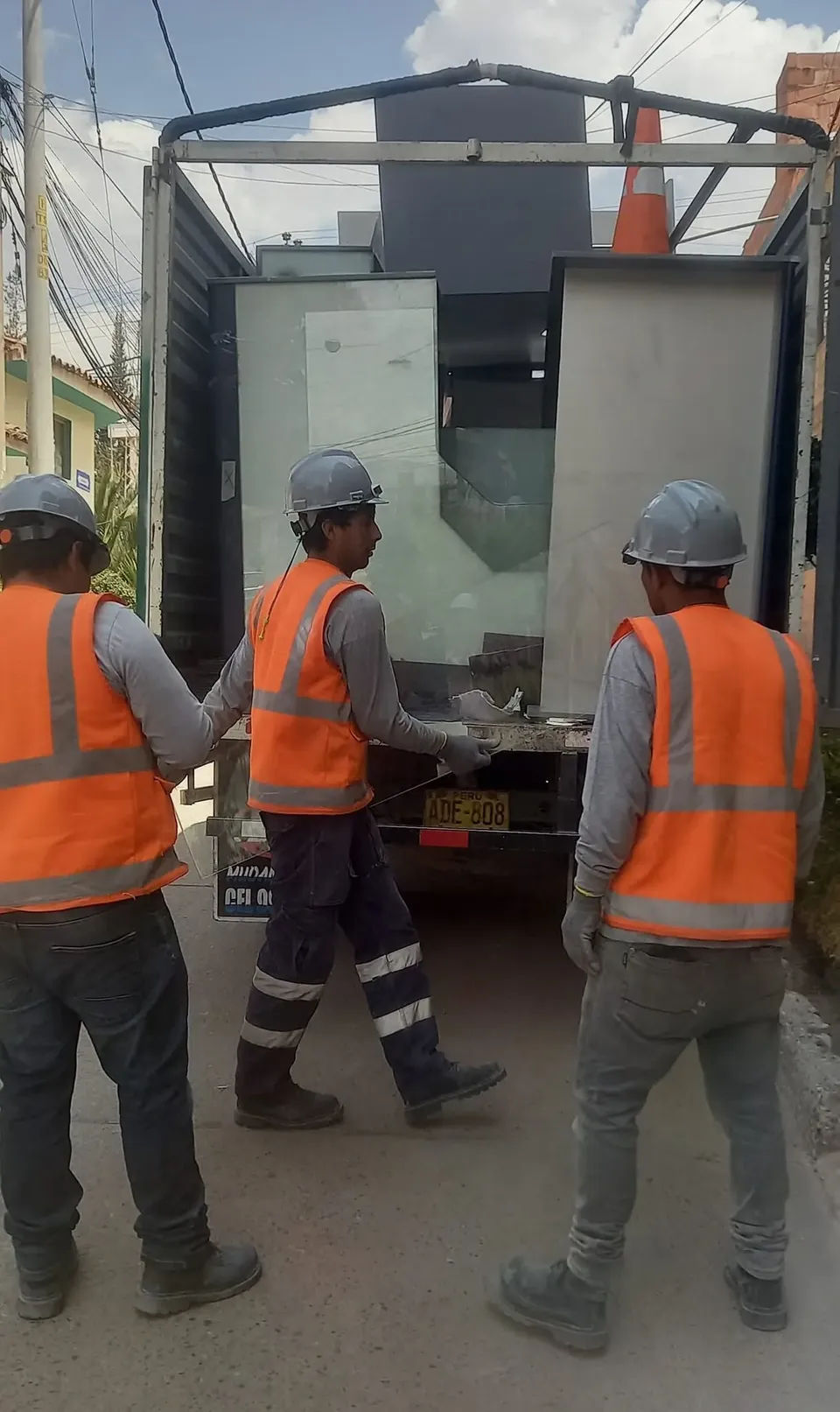 Tres cargadores con casco bajando paneles de vidrio de un camión