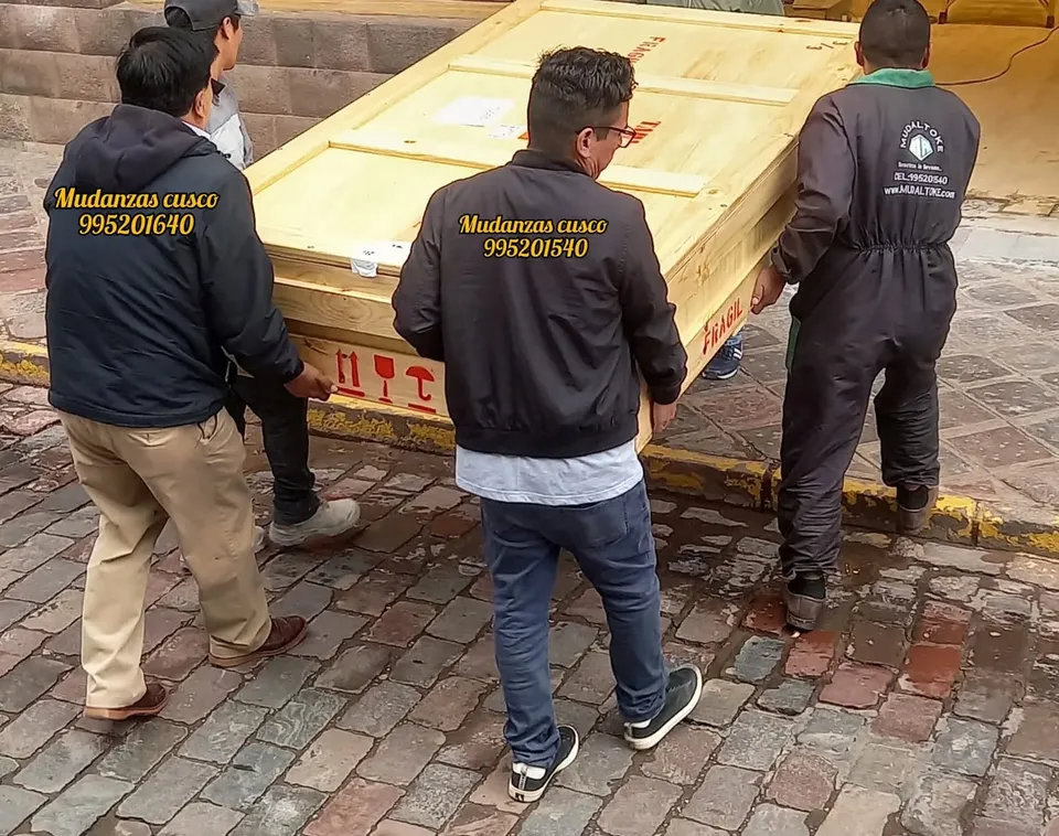 Cuatro cargadores llevando una caja de madera grande por una calle del centro de Cusco